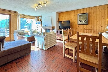 A cozy, wood-paneled living and dining room with tiled floors, a fireplace, and rustic wooden furniture.