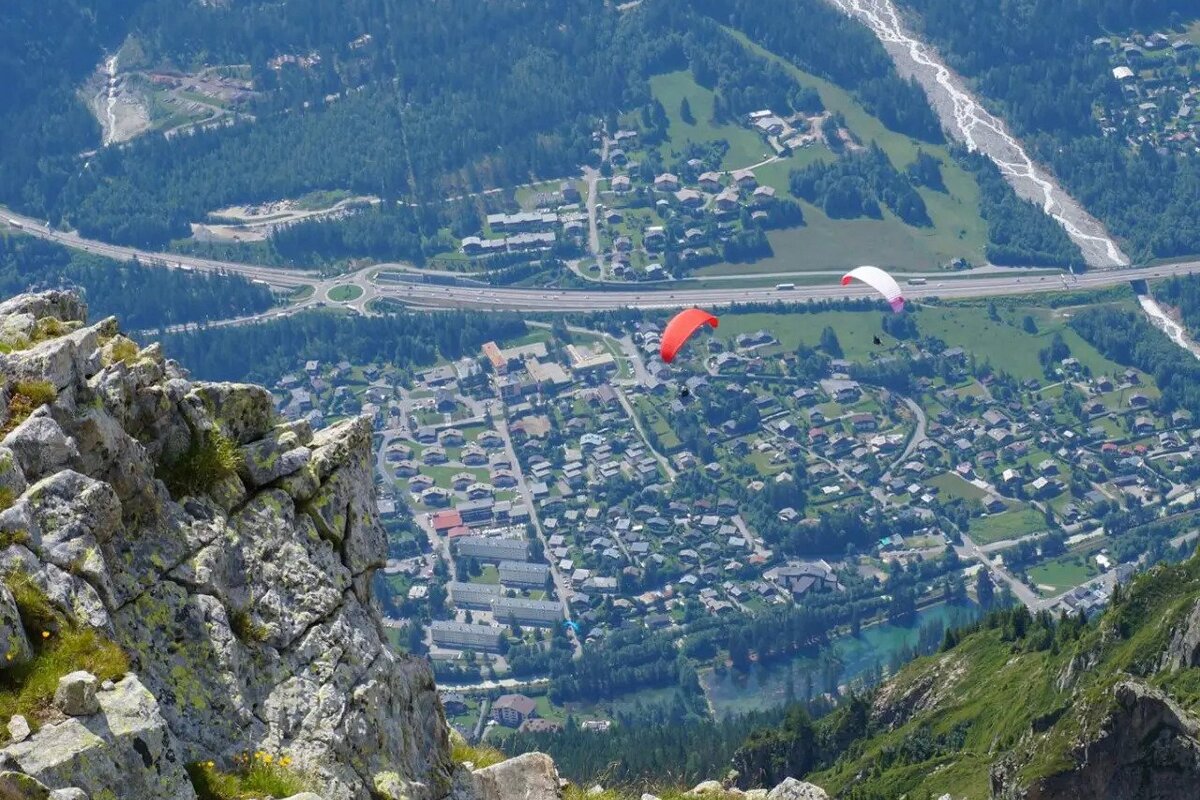 A paraglider flies over a small town in the mountains