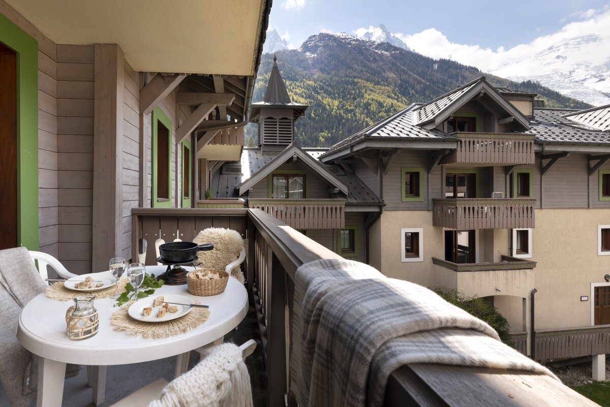 A balcony with a table and chairs and mountains in the background