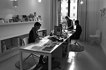 A black and white photo of a group of people sitting at desks in an office