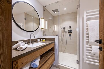 A modern bathroom featuring a wooden vanity, round mirror, and a glass-enclosed shower. Neutral tones create a clean, contemporary feel.