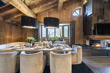 Cozy, rustic chalet dining room with a set breakfast table, stunning mountain views, a warm fireplace, and stylish black pendant lighting.