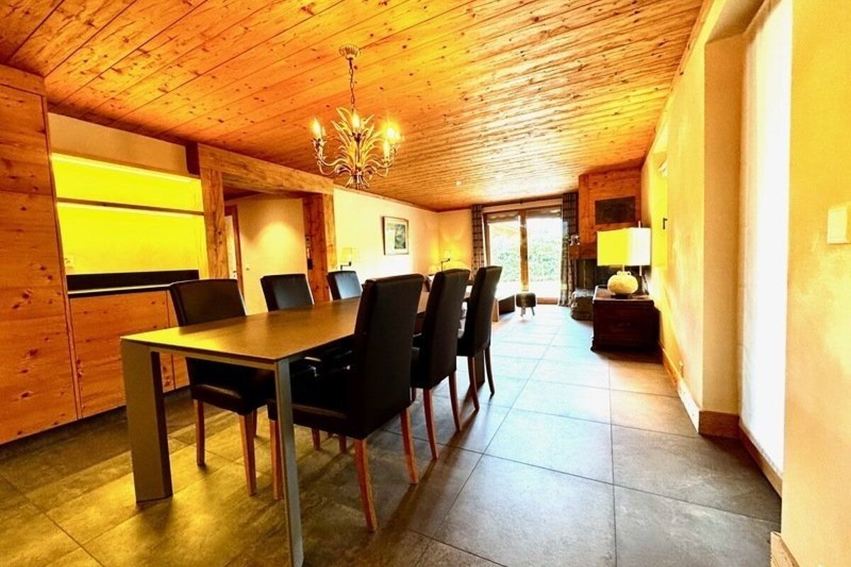 A cozy dining room with a wooden ceiling, a long dining table, and six black leather chairs.