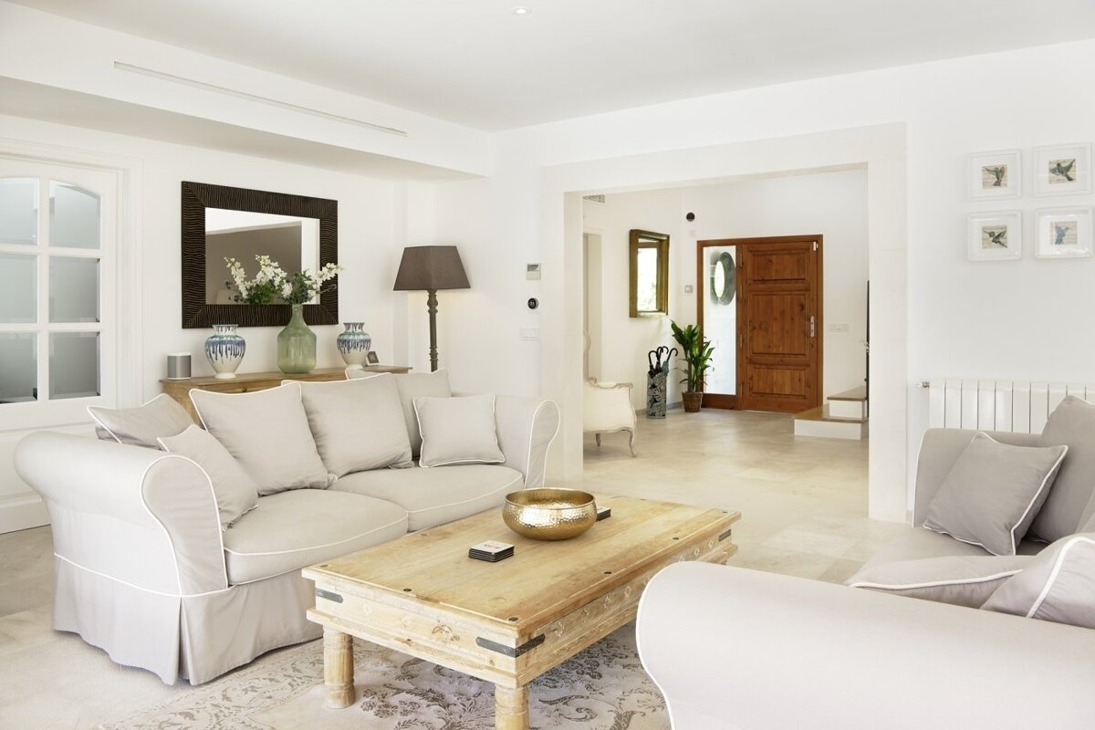 A bright, elegant living room with neutral-toned sofas, a rustic wooden coffee table, and an arched view into the entryway.