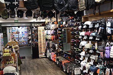 An indoor retail store displays numerous winter sports accessories like backpacks, helmets, goggles, beanies, sunglasses, and apparel.