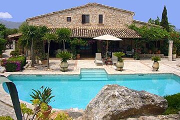 There is a large swimming pool in front of a large stone house