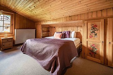 Cozy wood-paneled bedroom with a bed, purple bedding, a window, and a unique cabinet adorned with floral paintings.