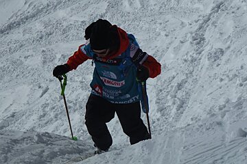 skier with 2 poles climbing back up a small slope