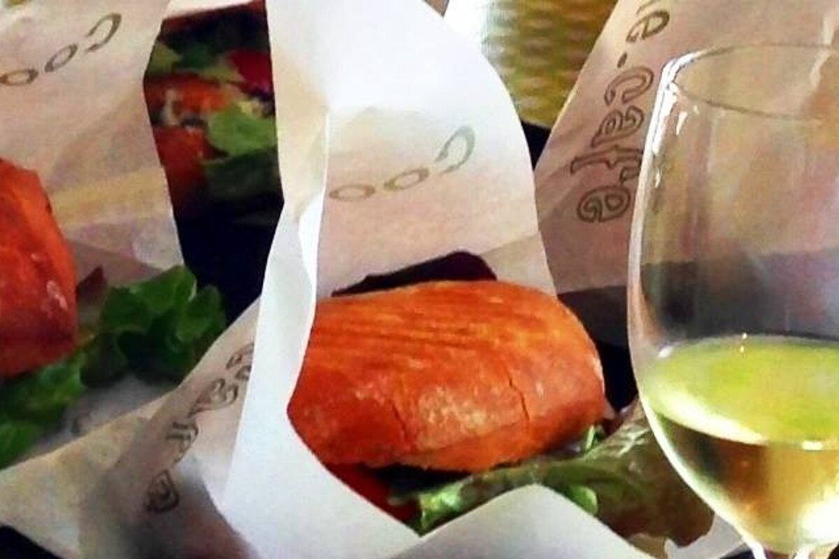 A glass of wine sits next to a sandwich wrapped in paper that says cafe