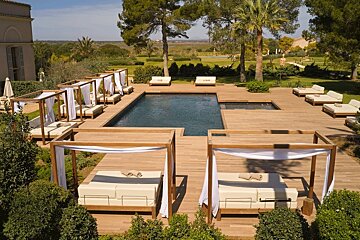 A luxurious resort pool area with a dark pool, expansive wooden deck, private cabanas, and sun loungers, surrounded by lush gardens.