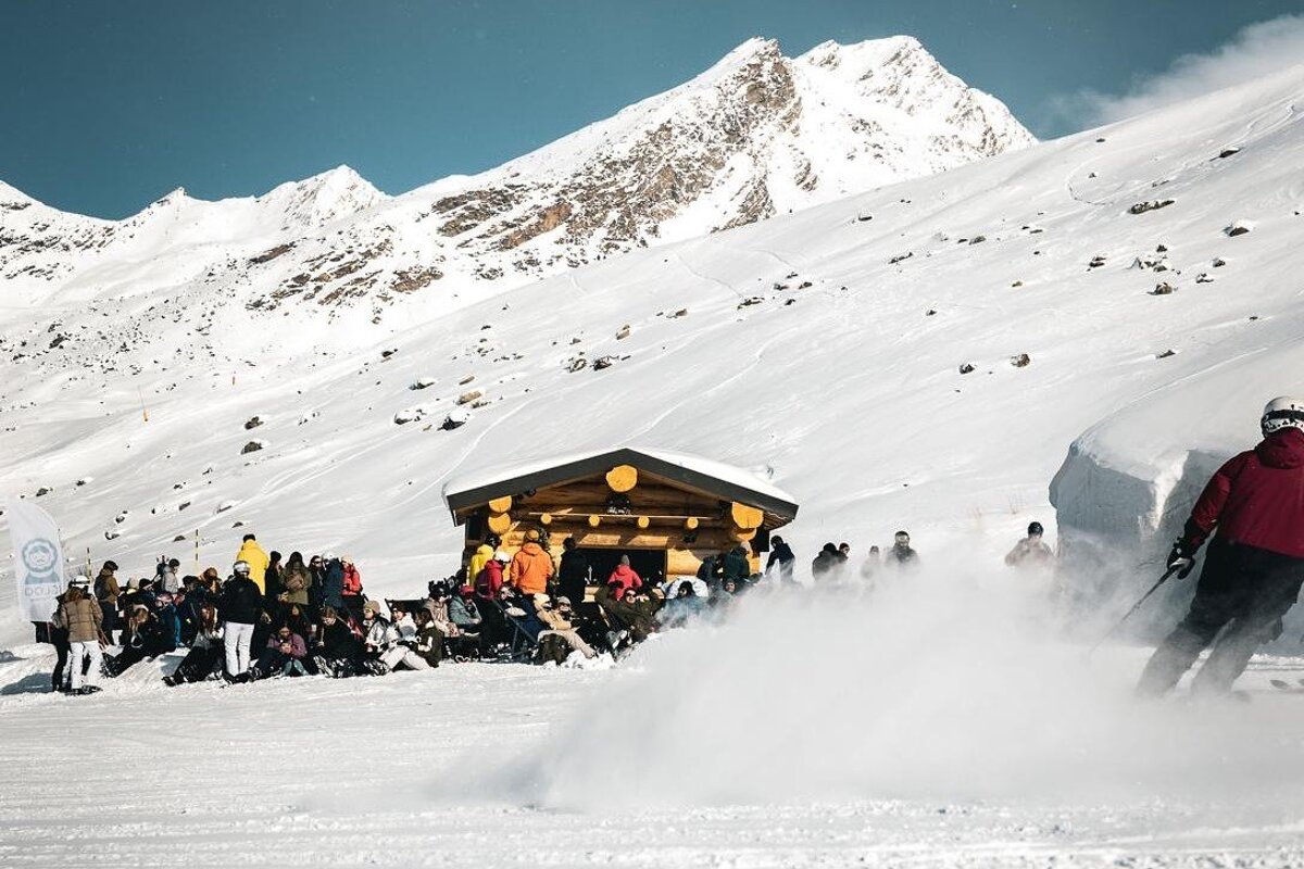 A group of people are gathered in the snow in front of a hut with a sign that says ' volkswagen ' on it