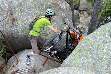 A man in a green shirt is carrying a bike on a ladder