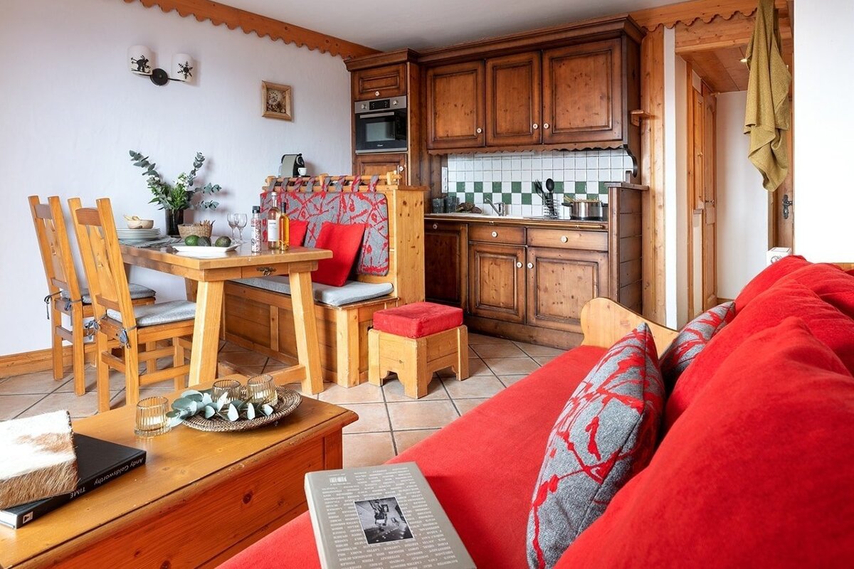 Cozy chalet interior featuring warm wooden cabinets, a dining area, and a bright red sofa in the foreground.
