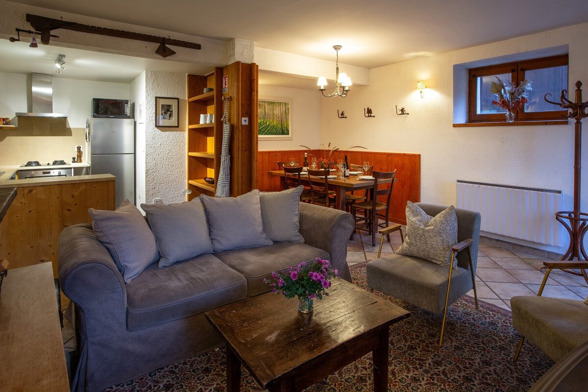 A warm and inviting open-plan living space featuring a gray sofa, a rustic coffee table, a dining area set for dinner, and a compact kitchen.