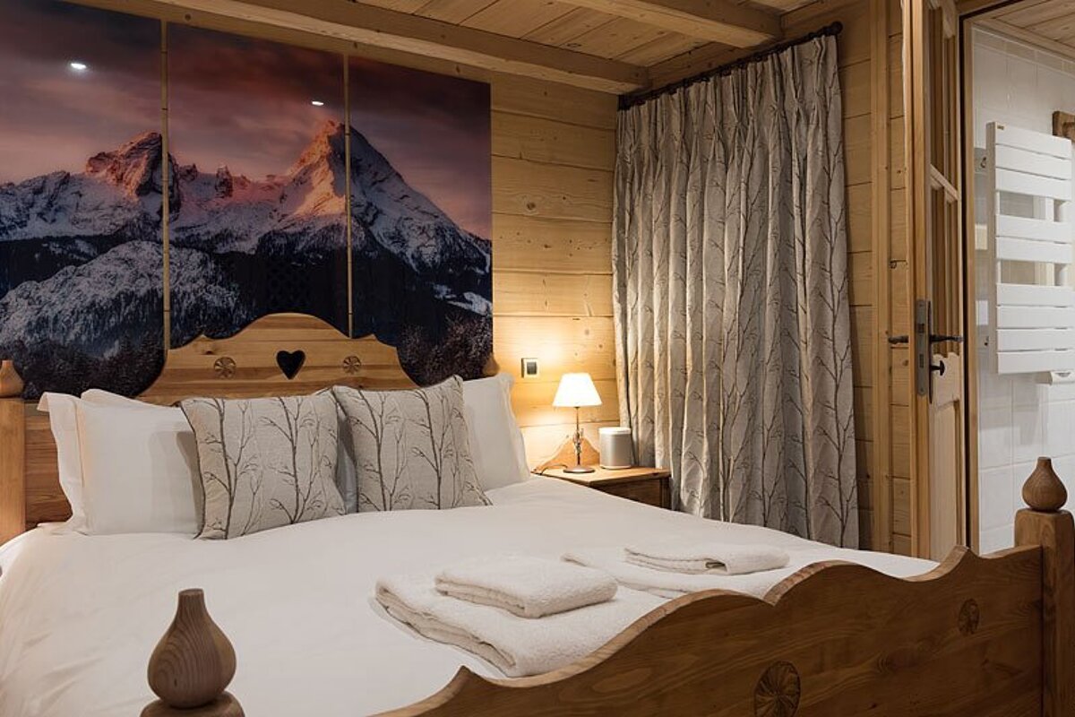A bedroom with a large picture of mountains on the wall above the bed