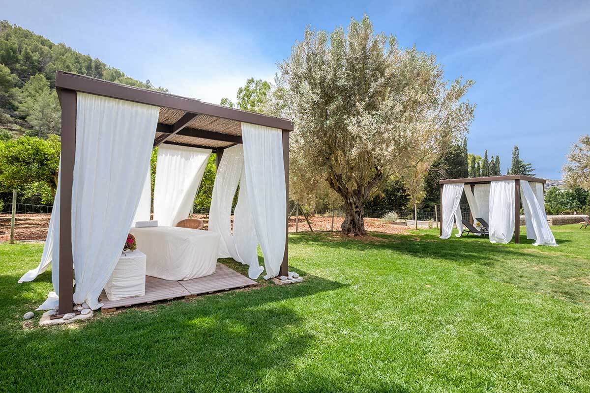 A gazebo with white curtains is in the middle of a lush green field