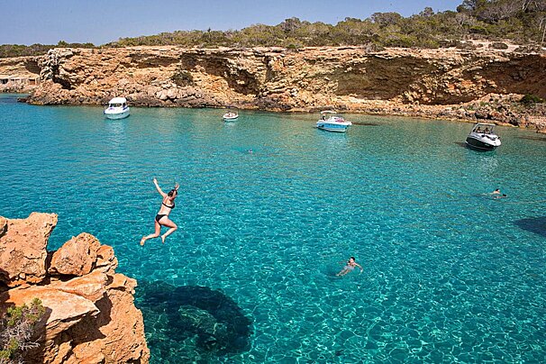 A woman jumps off a cliff into a body of water