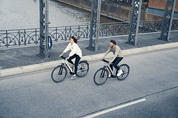 A man and a woman are riding bicycles on a bridge