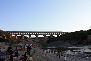 A group of people are gathered near a bridge over a river