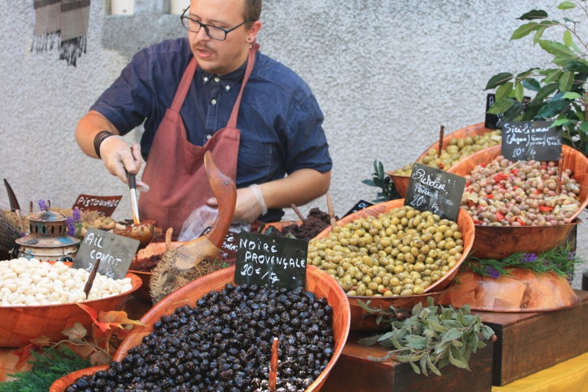 A man stands behind a display of olives with a sign that says noire provence