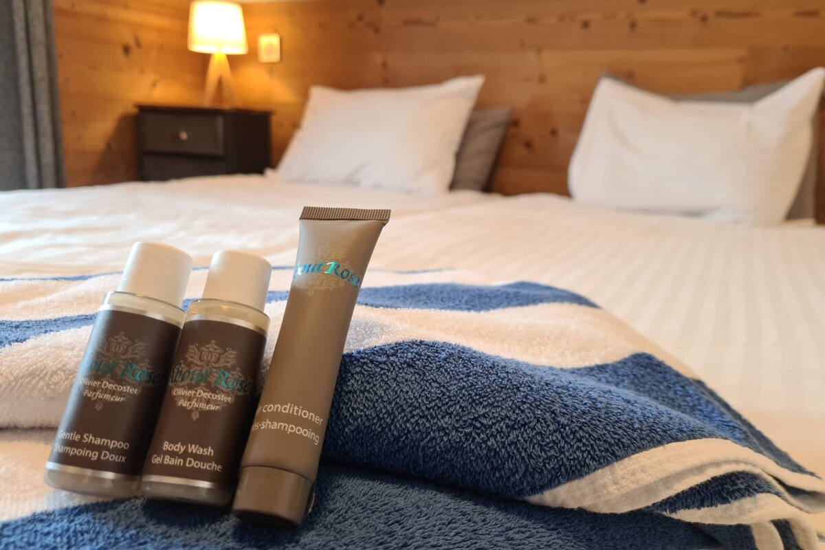 A bottle of conditioner sits on a bed next to a bottle of body wash