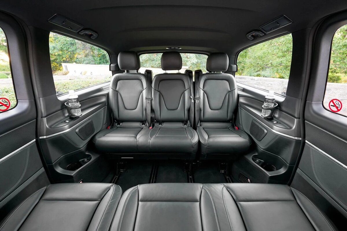 Luxurious black leather interior of a passenger van, featuring two rows of spacious seats, cup holders, and clear windows to an outdoor view.