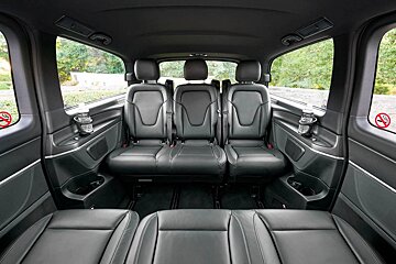 Luxurious black leather interior of a passenger van, featuring two rows of spacious seats, cup holders, and clear windows to an outdoor view.
