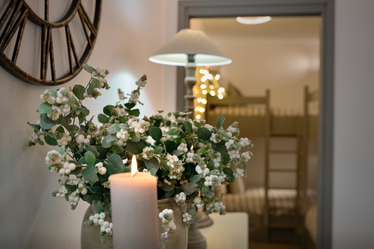 A vase of white flowers sits next to a lit candle