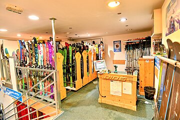 A well-lit ski and snowboard shop displaying many colorful skis and snowboards, along with ski poles, a wooden counter, and stairs.