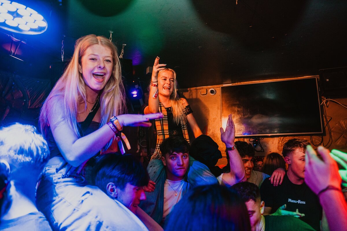 A man wearing a black t-shirt that says ' pleasure dome ' on it