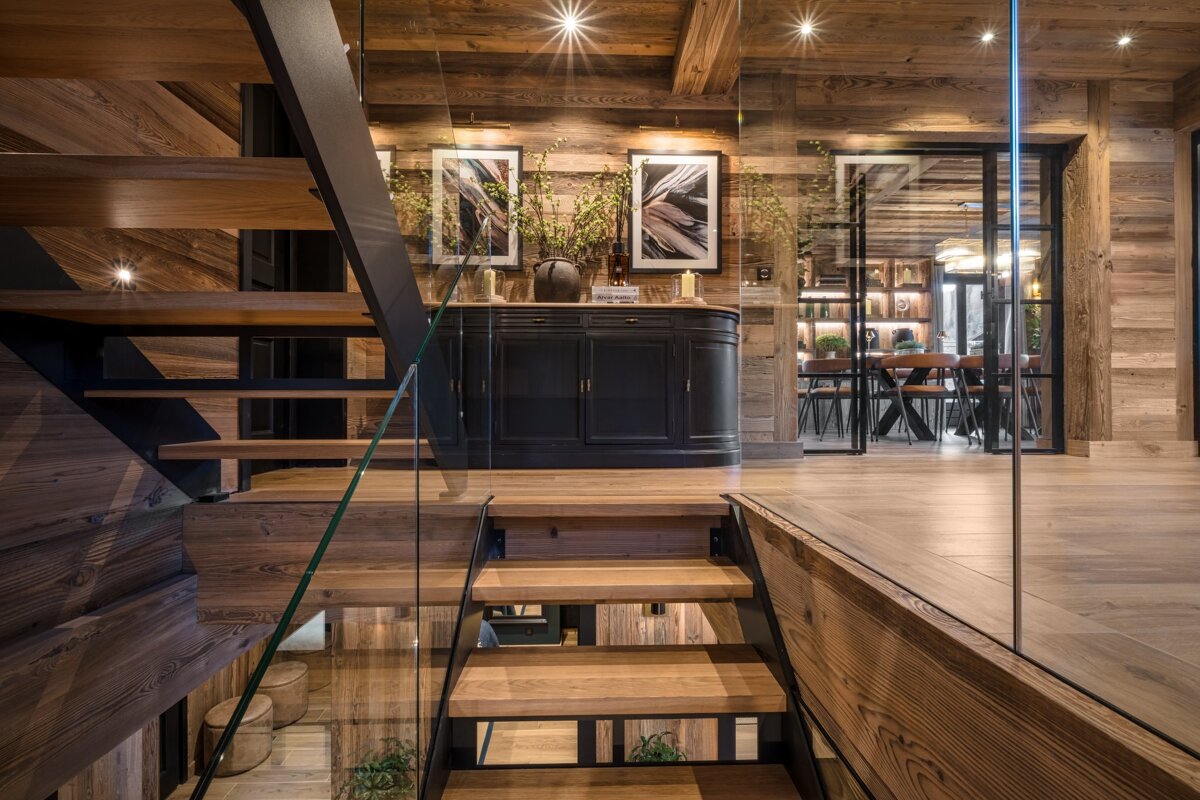 A wooden staircase with a glass railing leads to a dining room