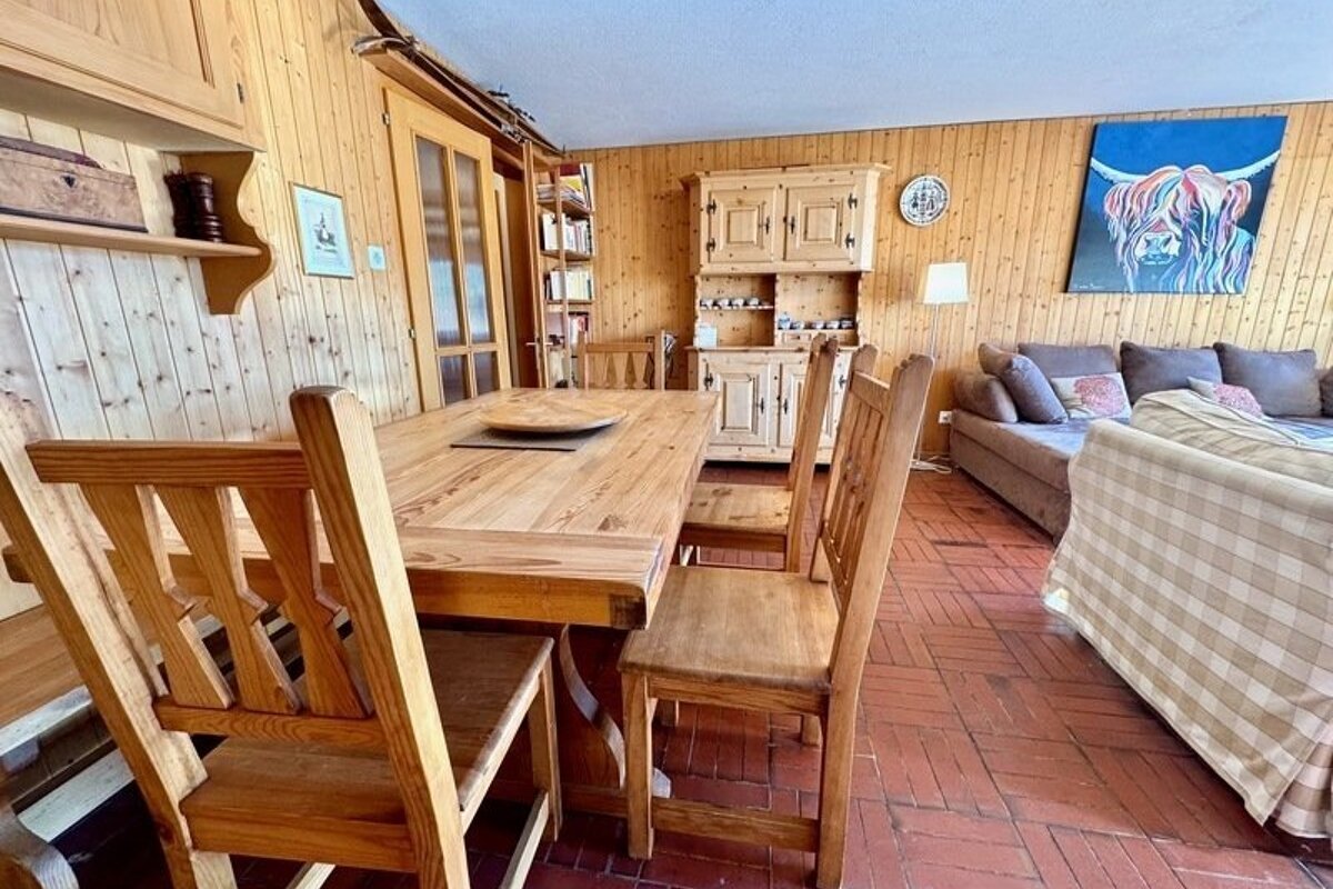 Rustic living space featuring wood-panelled walls, a dining set, tiled flooring, and a lounge area with a sofa.