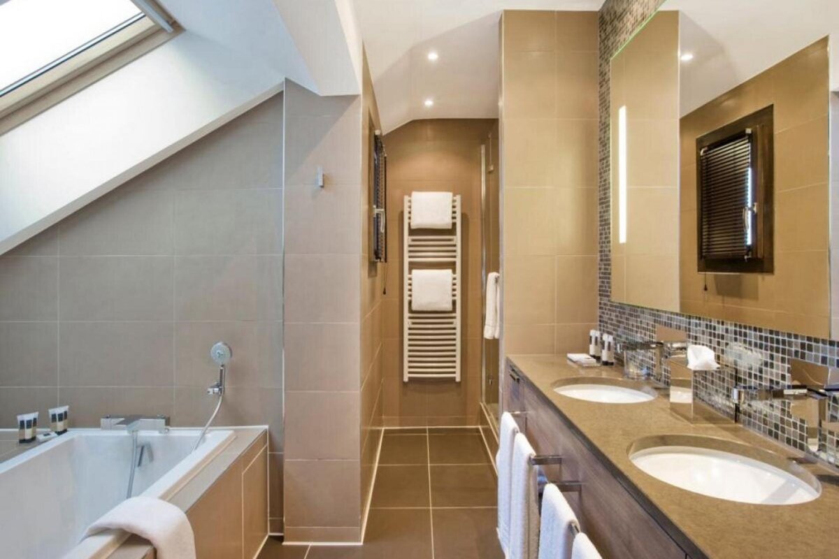 Modern, neutral-toned bathroom with a skylight over the tub, a separate shower, and a double vanity with two sinks.