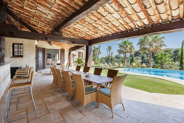 A table and chairs under a roof overlooking a swimming pool