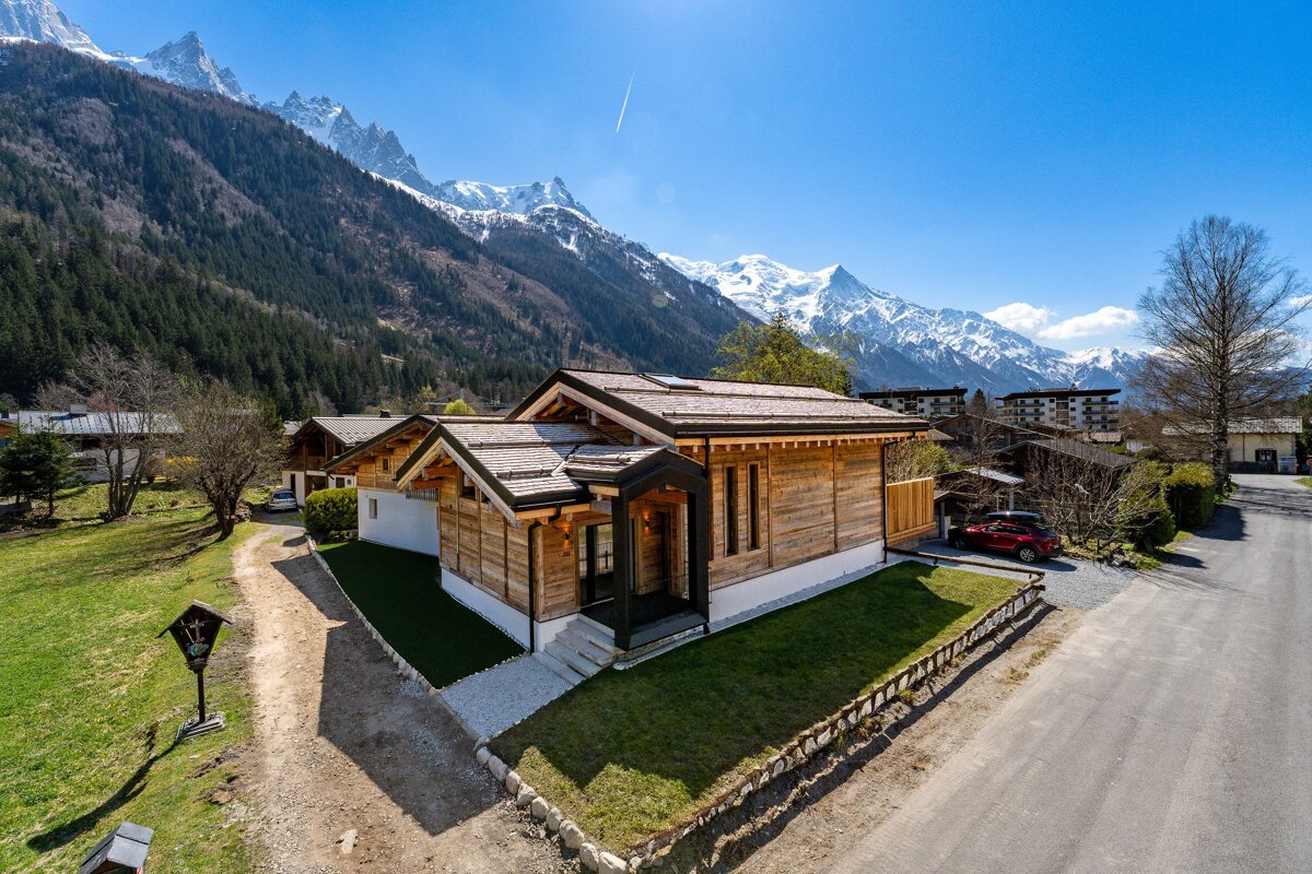 A red car is parked in front of a house with mountains in the background