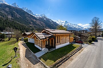 A red car is parked in front of a house with mountains in the background