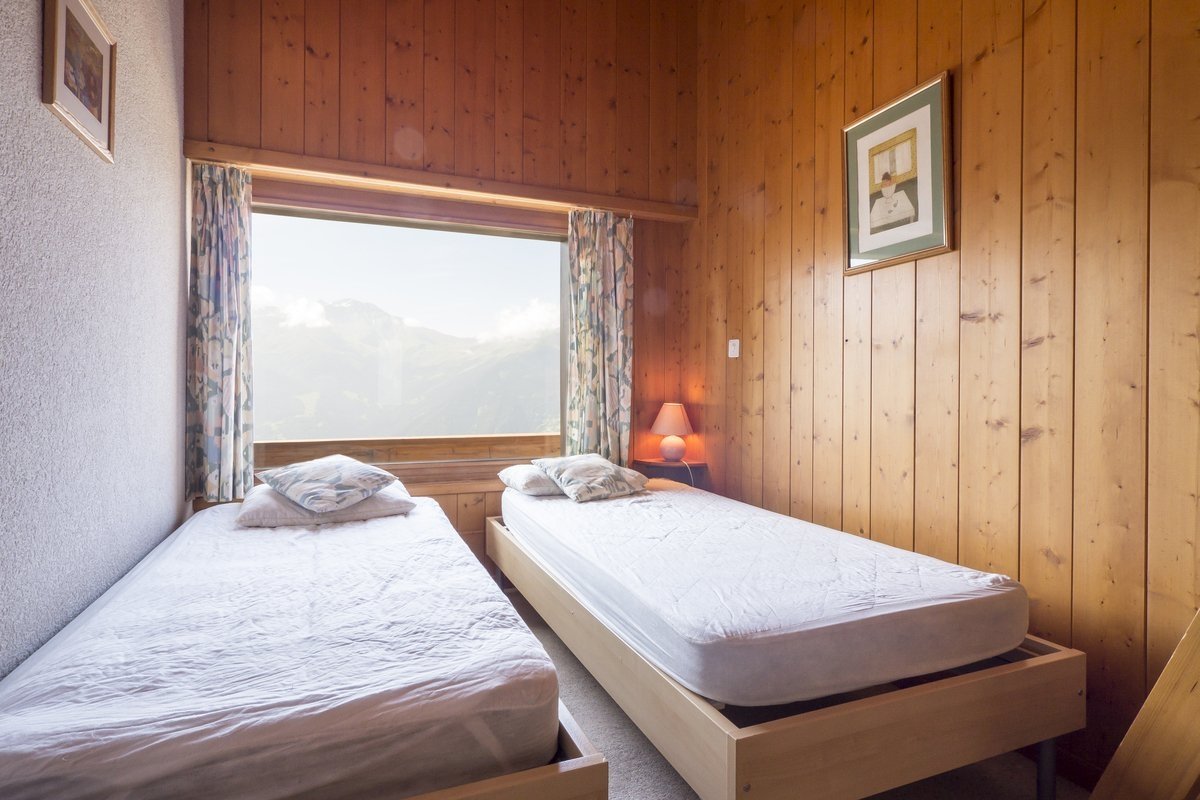 A cozy, wood-paneled bedroom with two twin beds and a large window looking out onto a scenic mountain view.