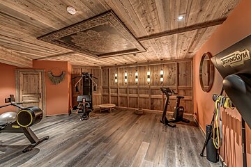 A luxurious home gym featuring rustic wood walls, ceiling, and floor, a peach accent wall, and modern fitness equipment.
