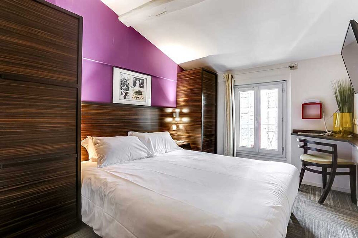 A hotel room with a purple wall and a white bed