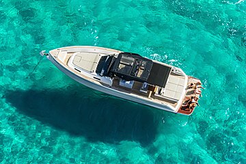 Aerial view of a luxury boat anchored in crystal-clear turquoise water, with people relaxing on the stern.