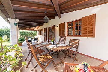 A table and chairs on a porch with shutters on the windows