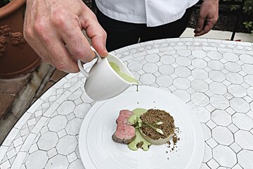 A person pouring green sauce on a plate of food
