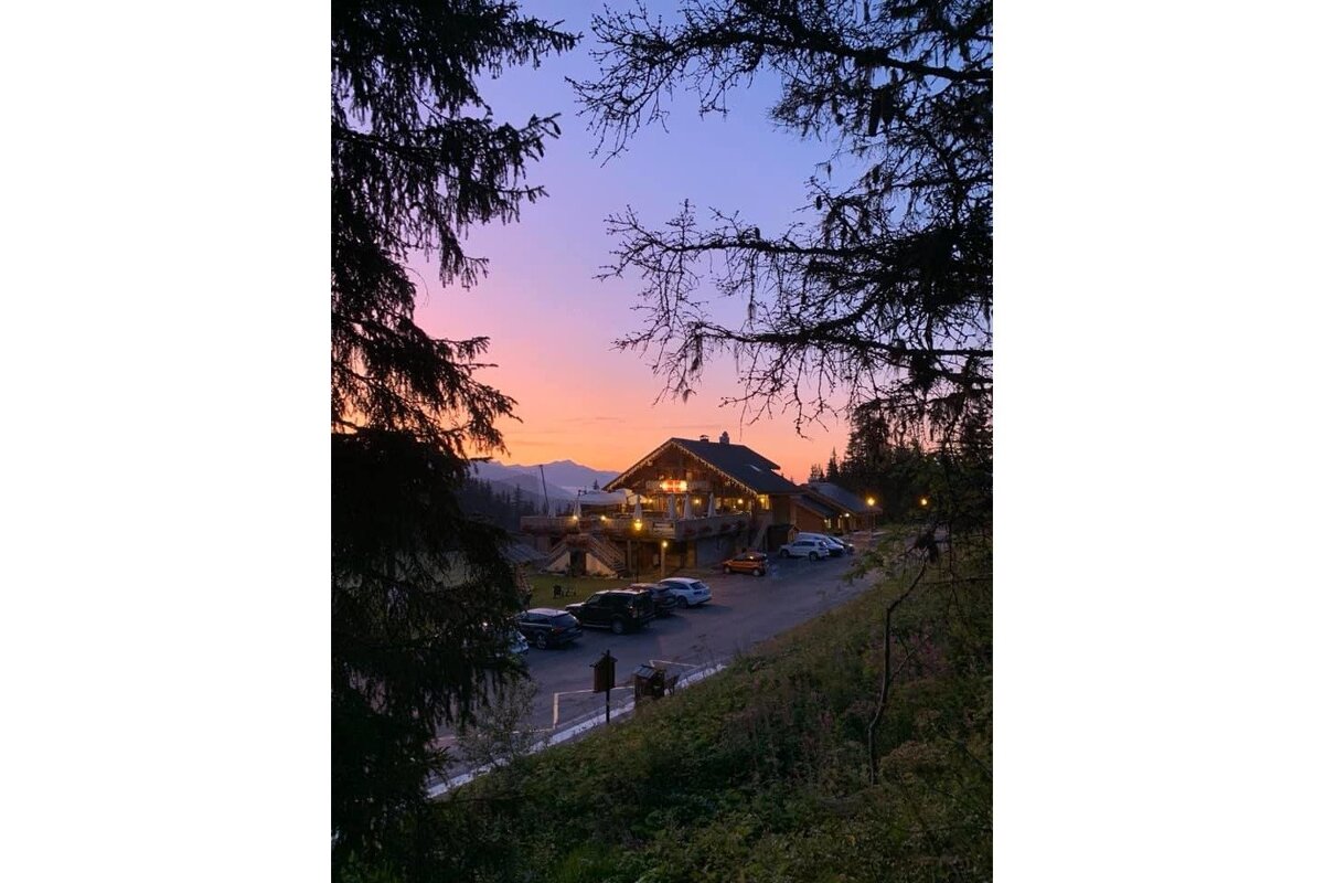 A sunset over a cabin with cars parked in front of it