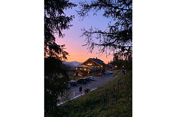 A sunset over a cabin with cars parked in front of it
