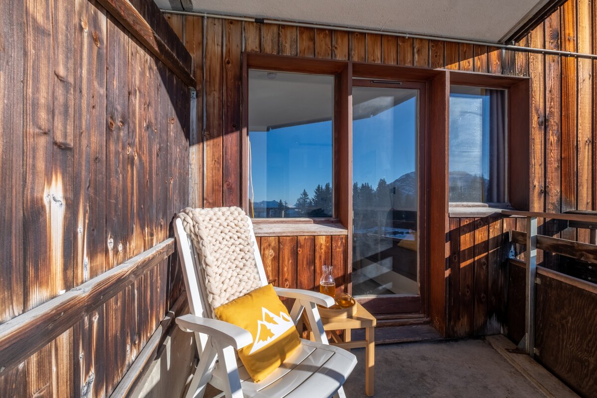 A chair with a yellow pillow with a mountain on it sits on a balcony