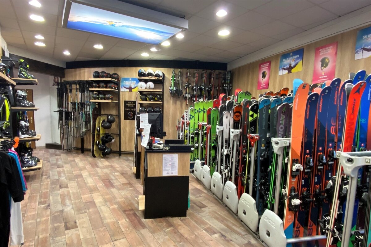 An indoor view of a well-stocked ski rental or retail shop, featuring rows of skis, snowboards, boots, helmets, and poles.