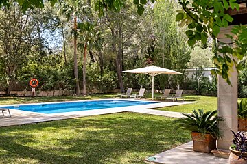 A large swimming pool is surrounded by a lush green lawn