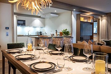 A stylish, open-plan dining room with a set table, leading to a modern kitchen and a cozy living area, creating an inviting atmosphere.