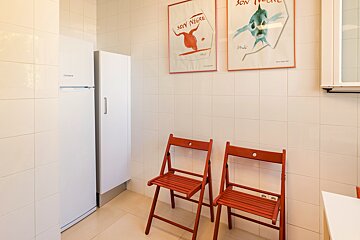 A white tiled room with a fridge, cabinet, two red folding chairs, and two framed graphic posters hanging on the wall.