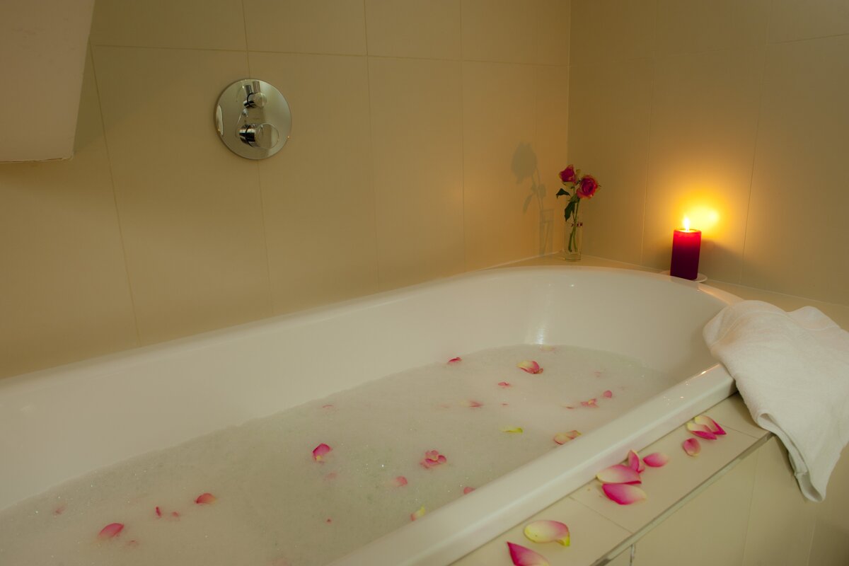 A bathtub filled with water and rose petals next to a candle